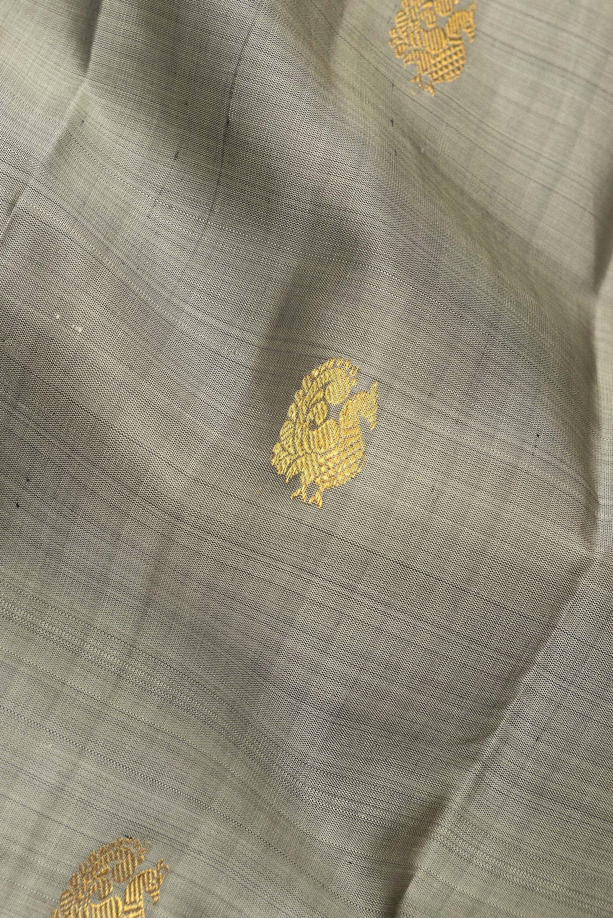 Close up of Pure Silk Grey Dual Tone Kanchipuram Saree with Zari Butta on the body and Zari Border.  displaying folds