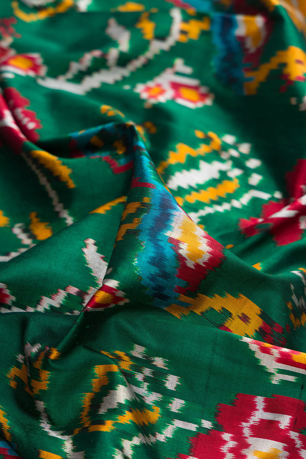 Close up of Pure Silk Bottle Green Dual Tone Double Ikat Saree with Ikat Print on the body and Ikat Border.  displaying folds