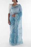 Woman wearing a light blue saree with white lace details on a white background