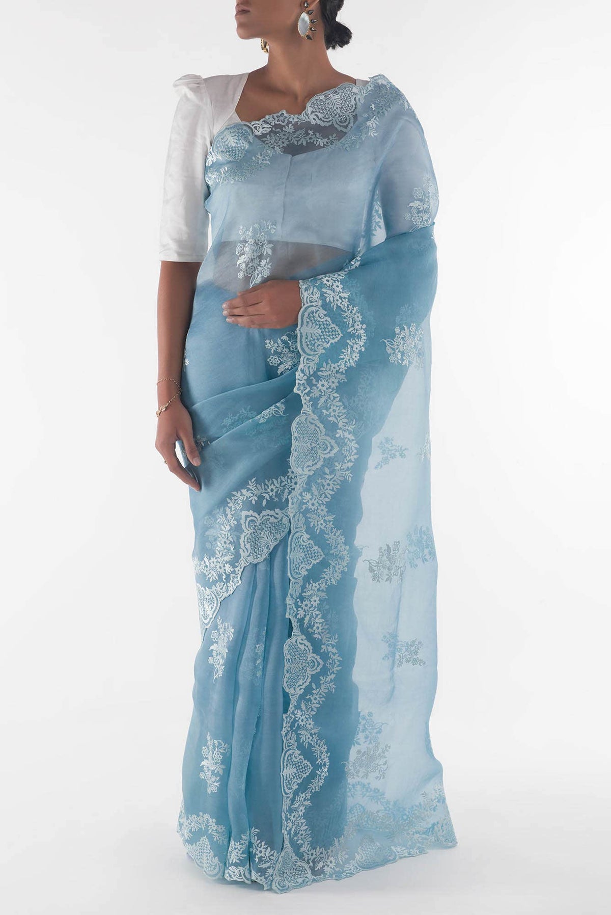 Woman wearing a light blue saree with white lace details on a white background
